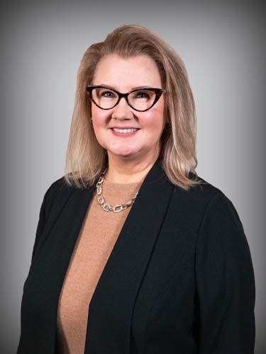 A woman wearing glasses and a black jacket is smiling for the camera.