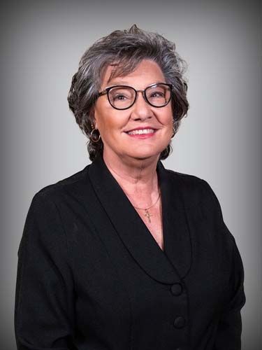 A woman wearing glasses and a black jacket is smiling for the camera.