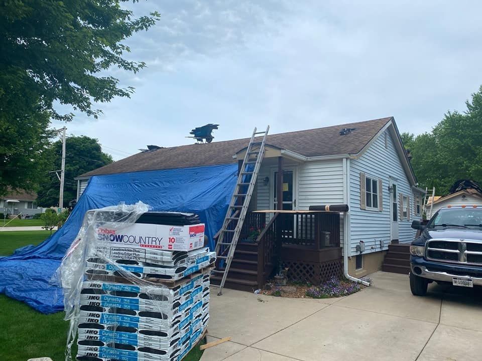A truck is parked in front of a house with a blue tarp on the roof.