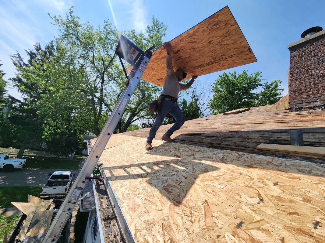 A man is carrying a piece of plywood on top of a roof.