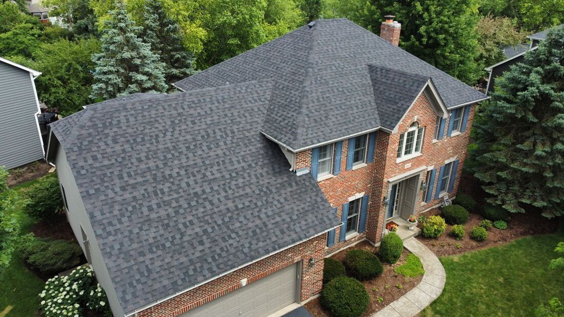 An aerial view of a large brick house with a new roof.