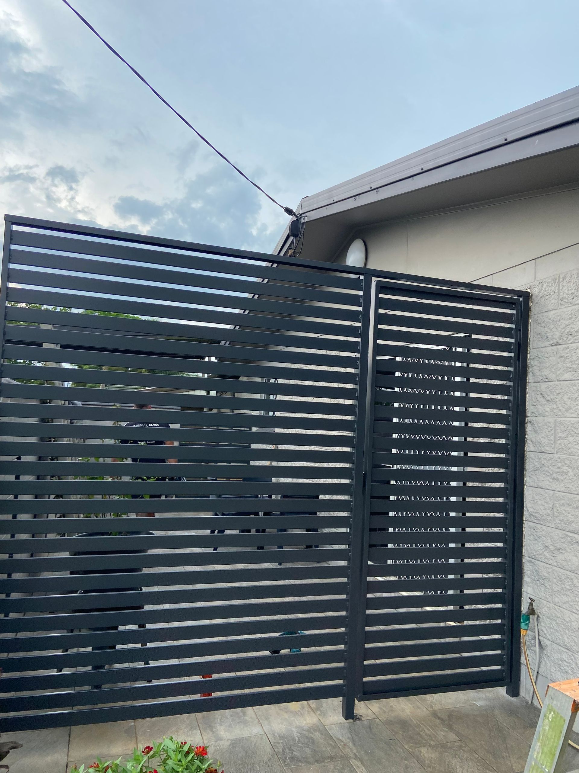 Black Horizontal Slat Gate Against a Beige Wall and Cloudy Sky — Innisfail Glass & Aluminium in Innisfail, QLD