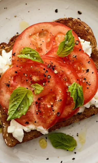 A close up of a slice of toast with tomatoes and basil on a plate.