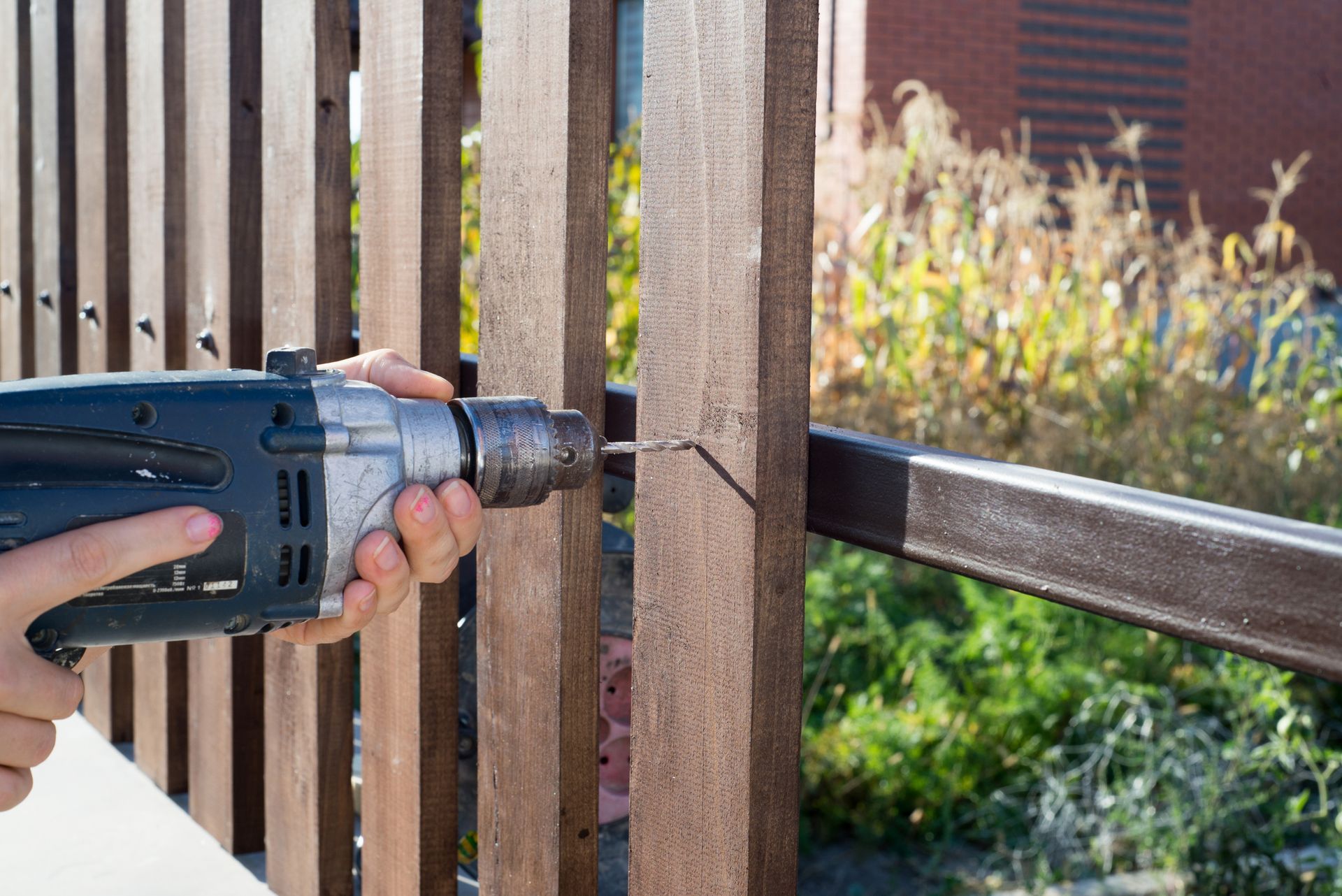 Fence contractor drilling a wood plank fence to a metal frame, building a wooden fence with a drill Fence contractor drilling a wood plank fence to a metal frame, building a wooden fence with a drill