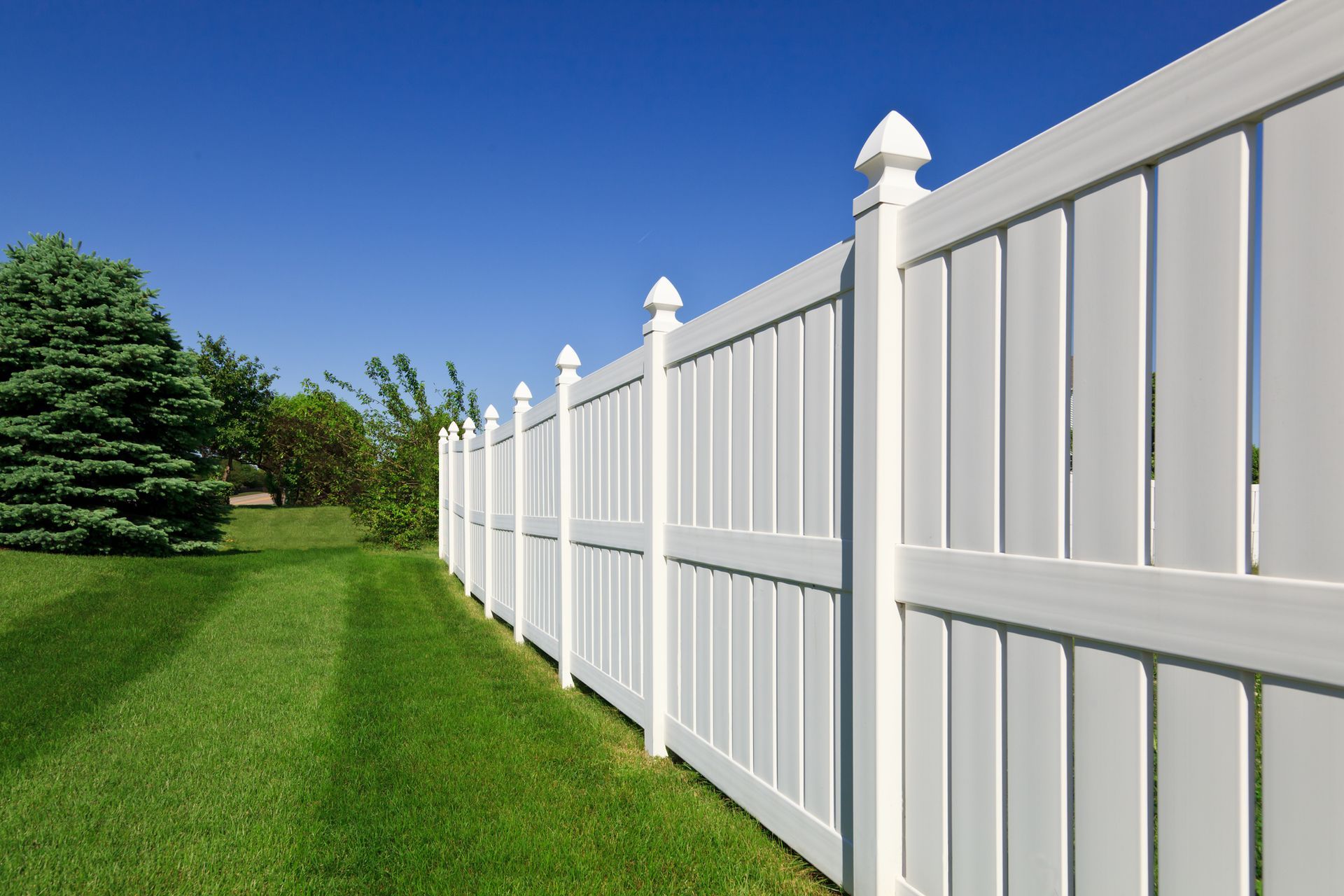 White vinyl privacy fence installed by a professional fence contractor in a green yard. 