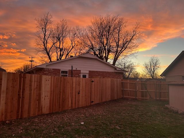 A wooden fence in front of a house with a sunset in the background.