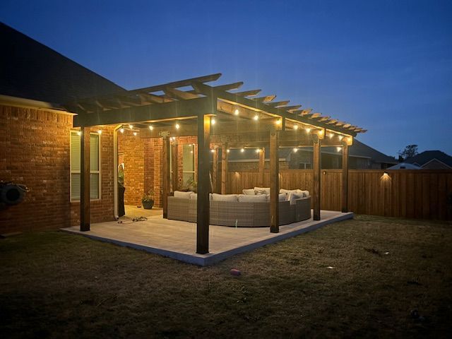 A pergola with a couch underneath it is lit up at night.