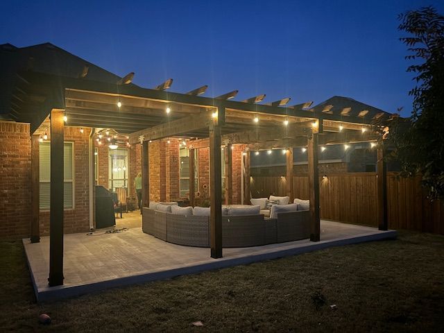 A patio with a pergola and string lights is lit up at night.