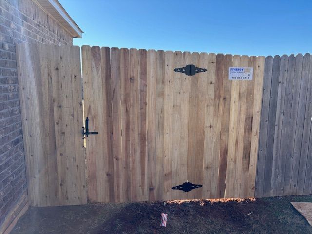 A wooden fence with a gate and a brick building in the background.