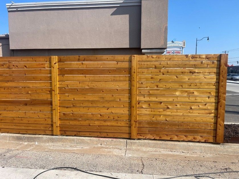 Wooden fence along a sidewalk in front of a building on a sunny day.