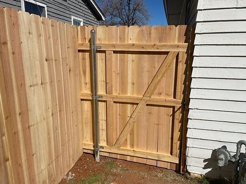 A wooden fence with a metal gate is next to a white house.