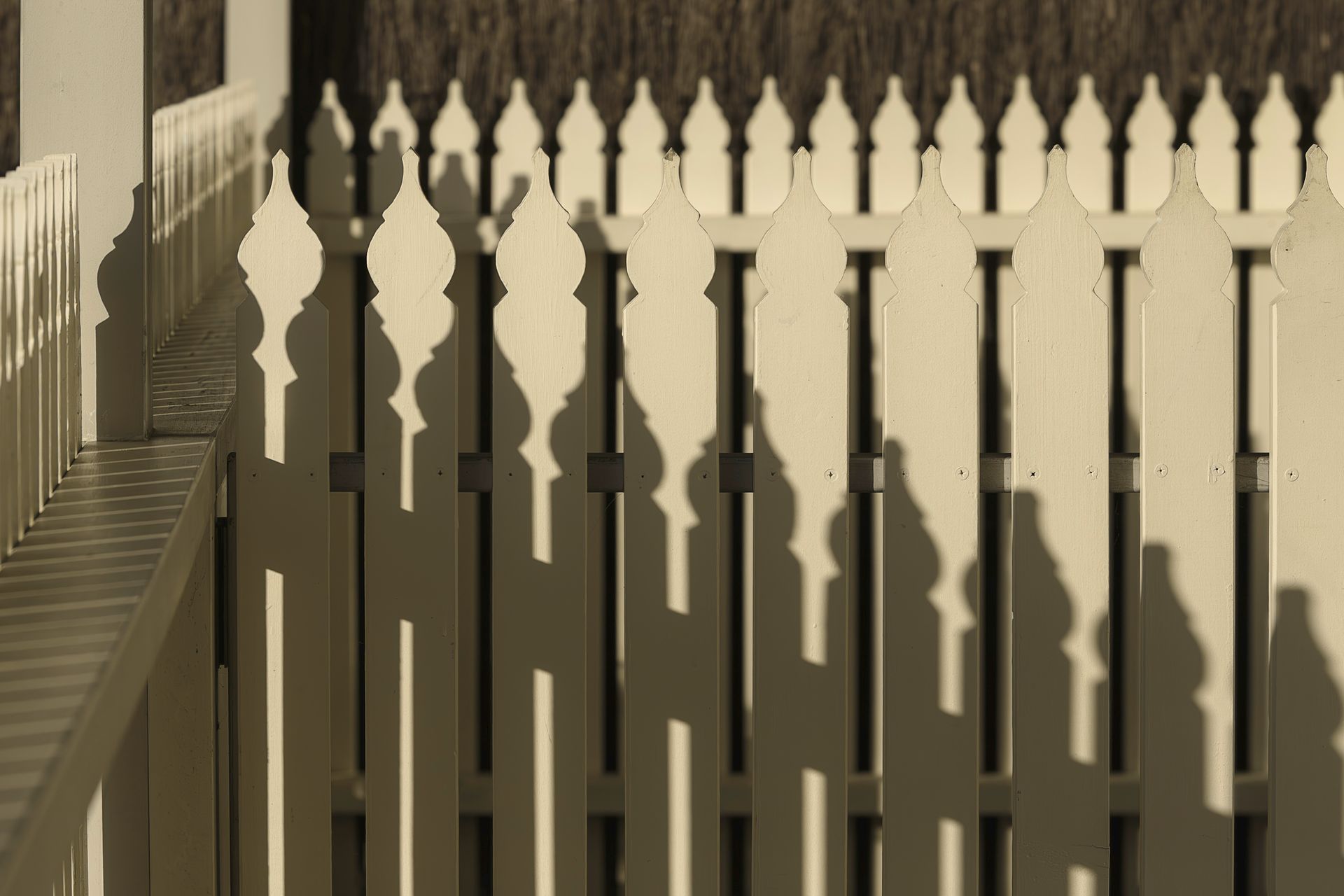 Close-up of white picket fence with shadows in sunlight.