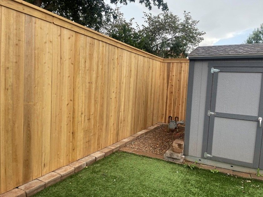 Wooden fence surrounds a yard with a shed, artificial grass, and gravel.