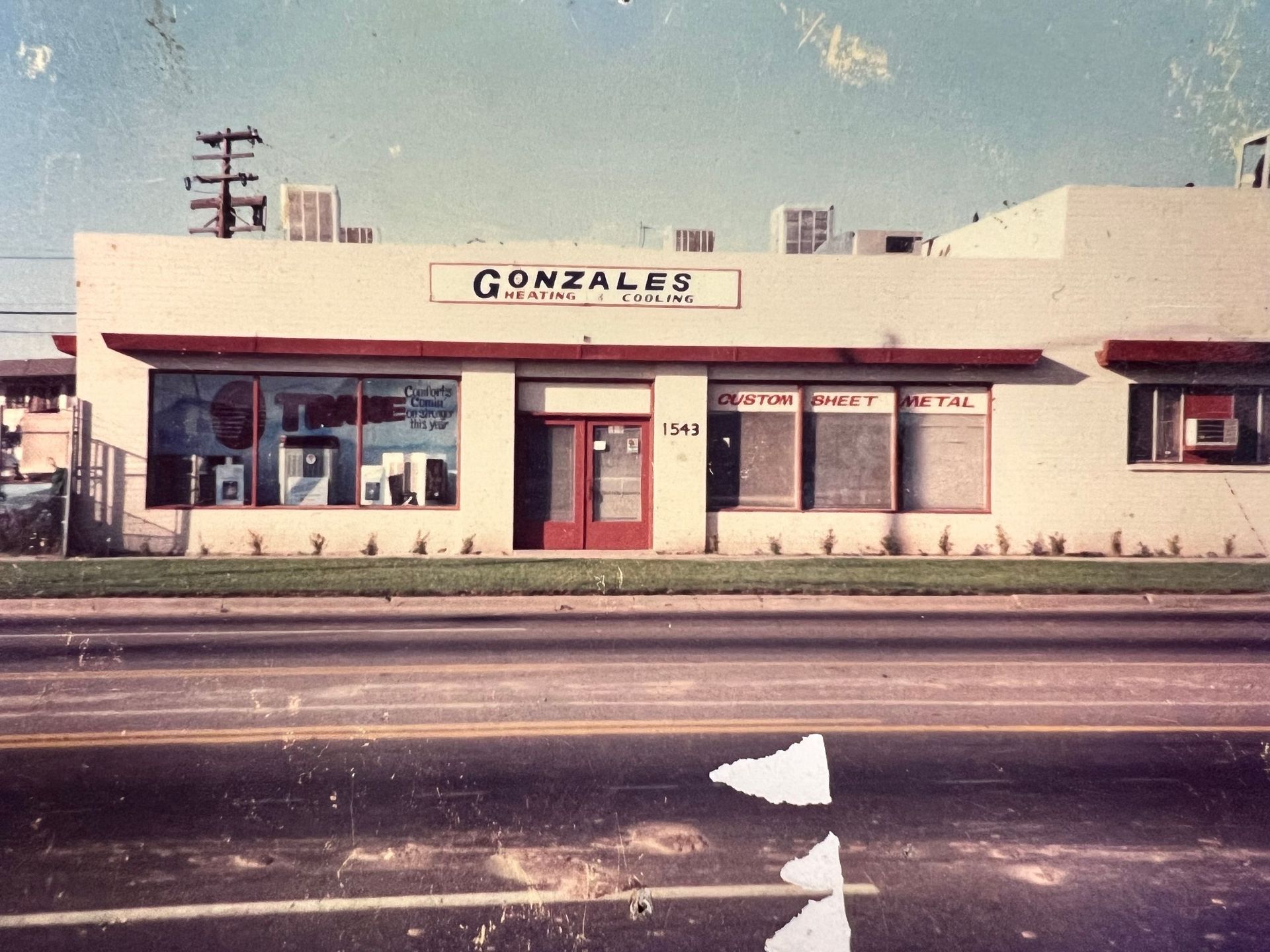Exterior of Gonzales Printing and Office Supplies in a one-story building with a red door and display windows. The street reflects the building.