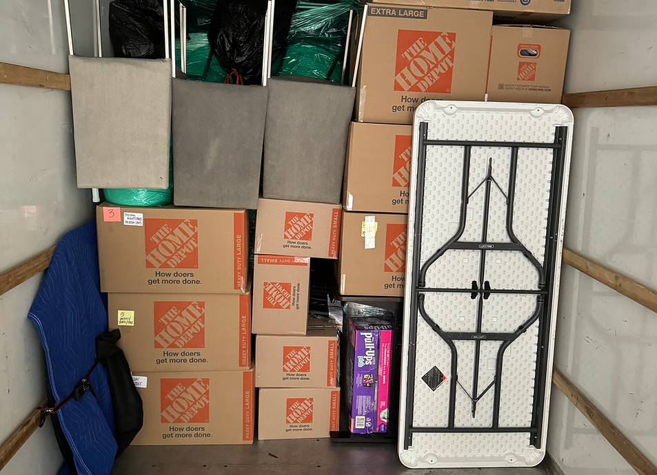 Inside a moving truck: boxes, a folding table, upholstered chairs, and furniture pads.