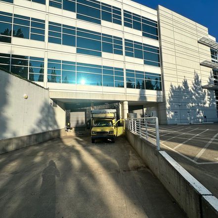 Yellow van under modern building with reflective windows. Shadow of person in foreground.