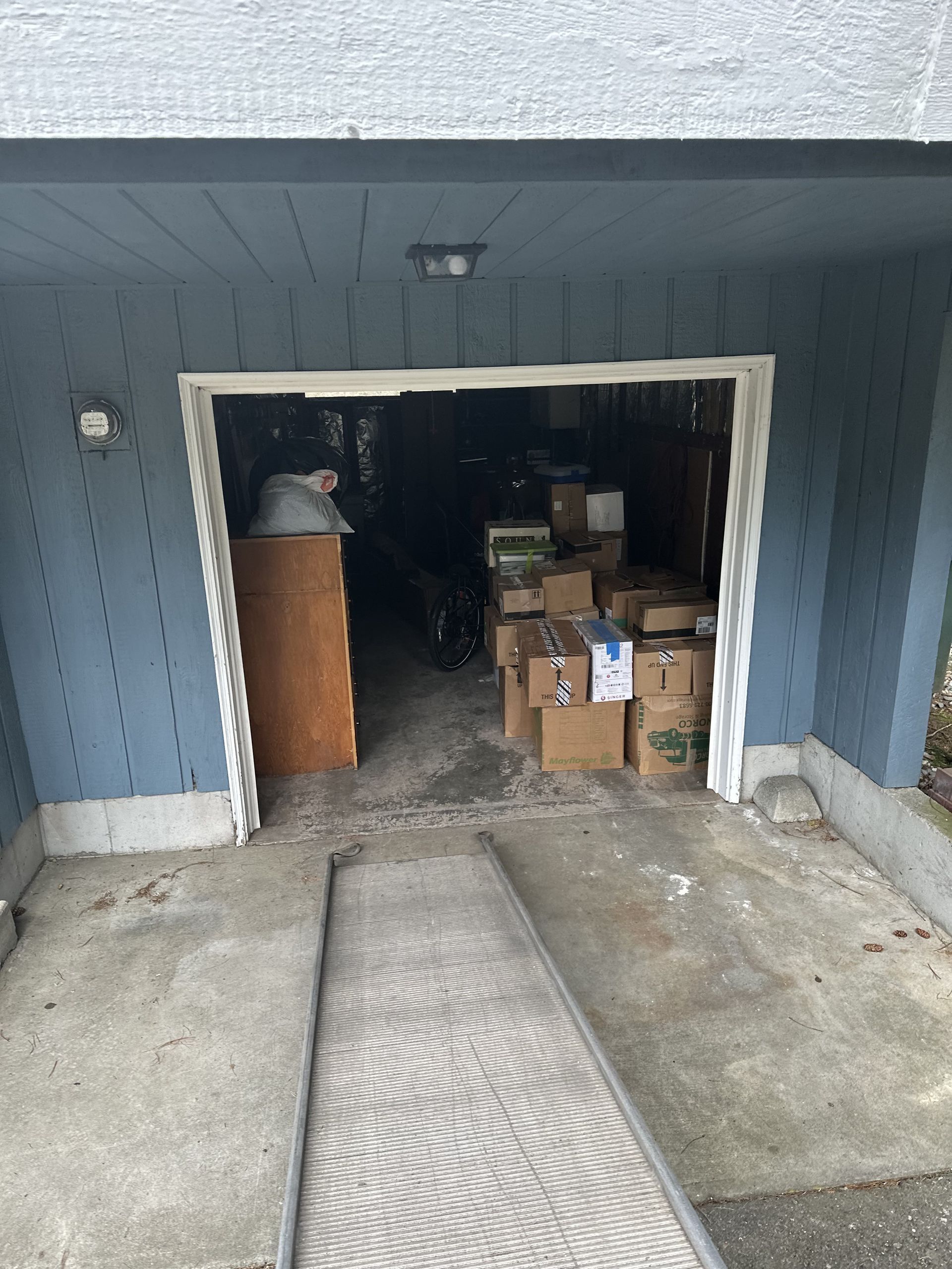 Garage interior filled with boxes. Light-colored entrance with ramp. Blue exterior wall.