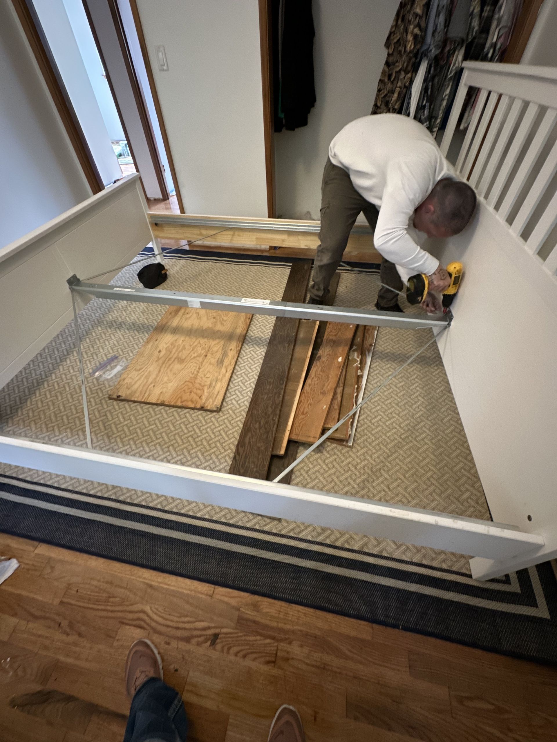 Person assembles white crib frame in a room with hardwood floors and rug.