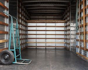 Inside of a cargo truck with a teal hand truck on the left.