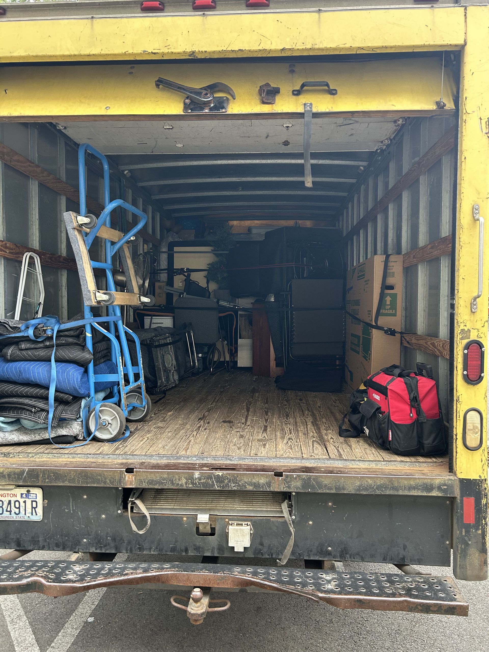 Interior of a yellow moving truck, partially loaded with furniture, moving blankets, boxes, and a blue hand truck.