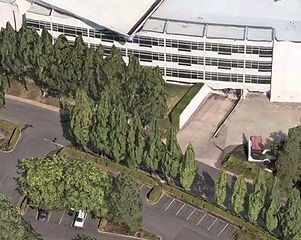 Aerial view of a multi-story building with a parking lot in the foreground. Green trees line the building's edge.