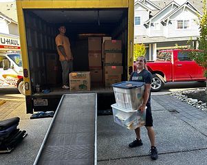 Two men loading a U-Haul truck with boxes and bins in front of a house.