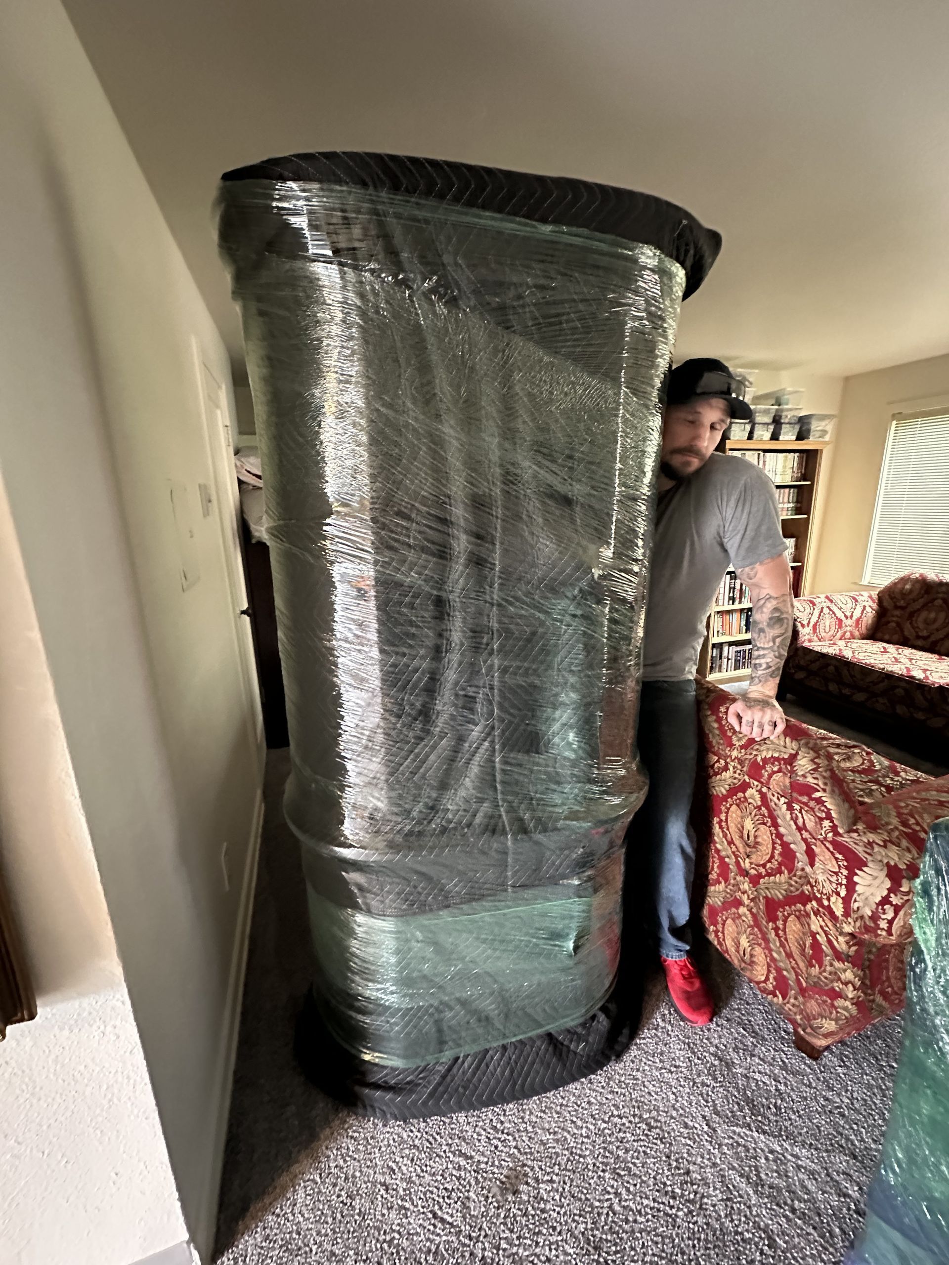 Man pushing a large, wrapped item, possibly furniture, down a hallway.