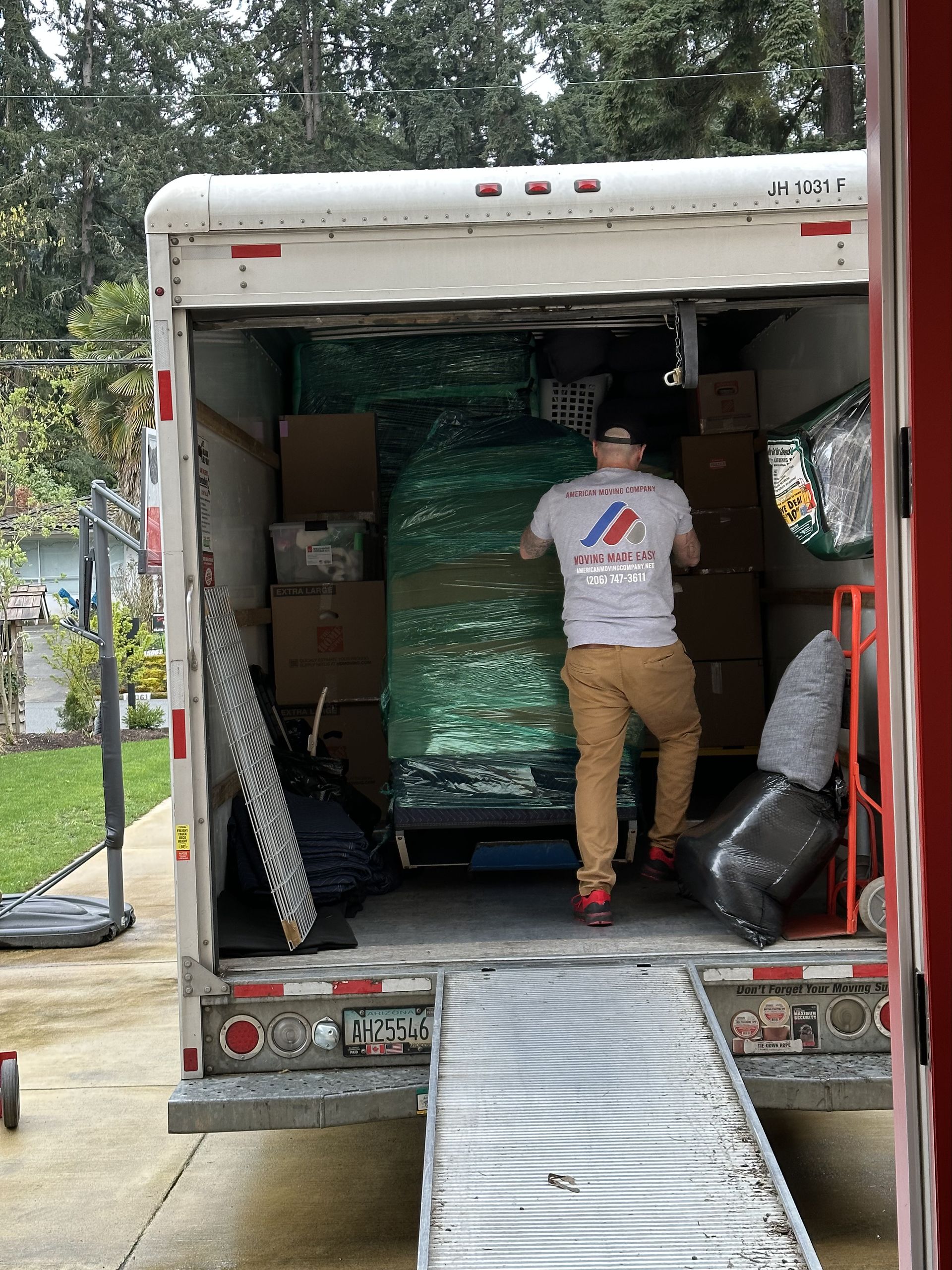 Man loading a moving truck with boxes and wrapped furniture; outdoors on a driveway.