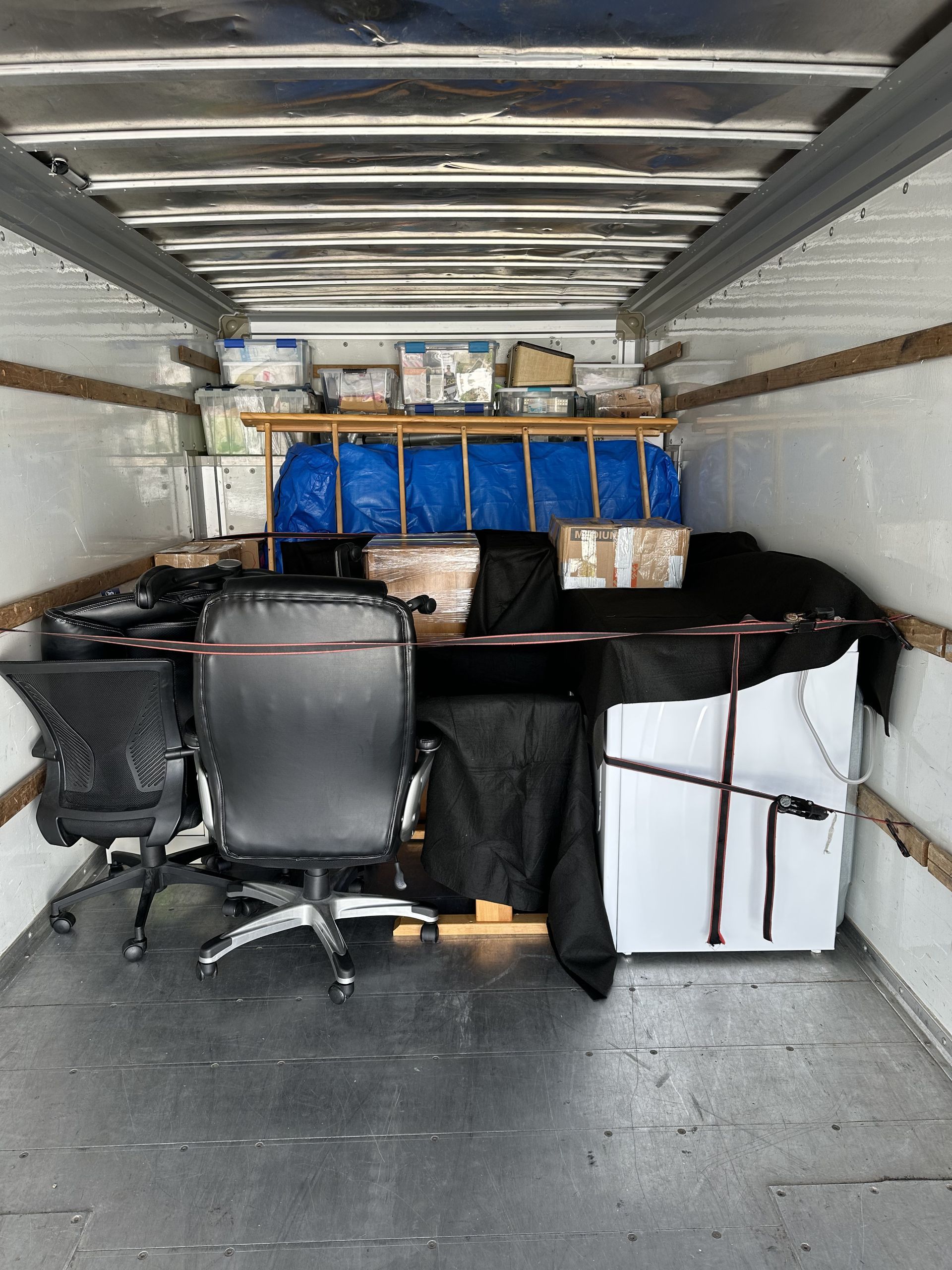 Inside of a moving truck filled with boxes, chairs, and other items.