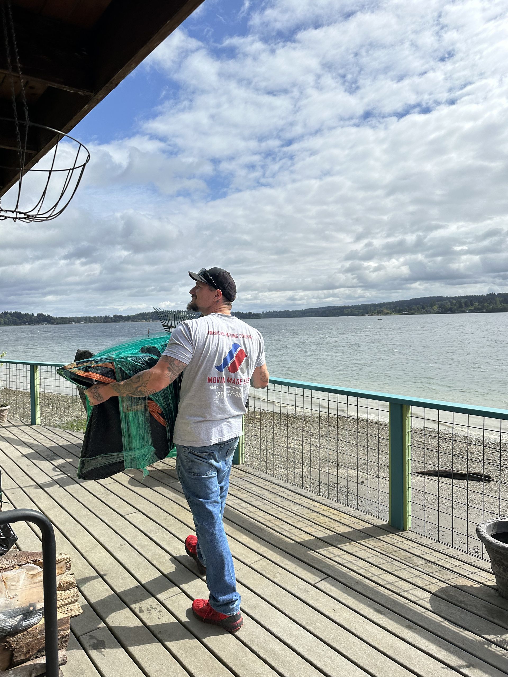 Man on a wooden deck, carrying a fishing net towards a lake under a cloudy sky.