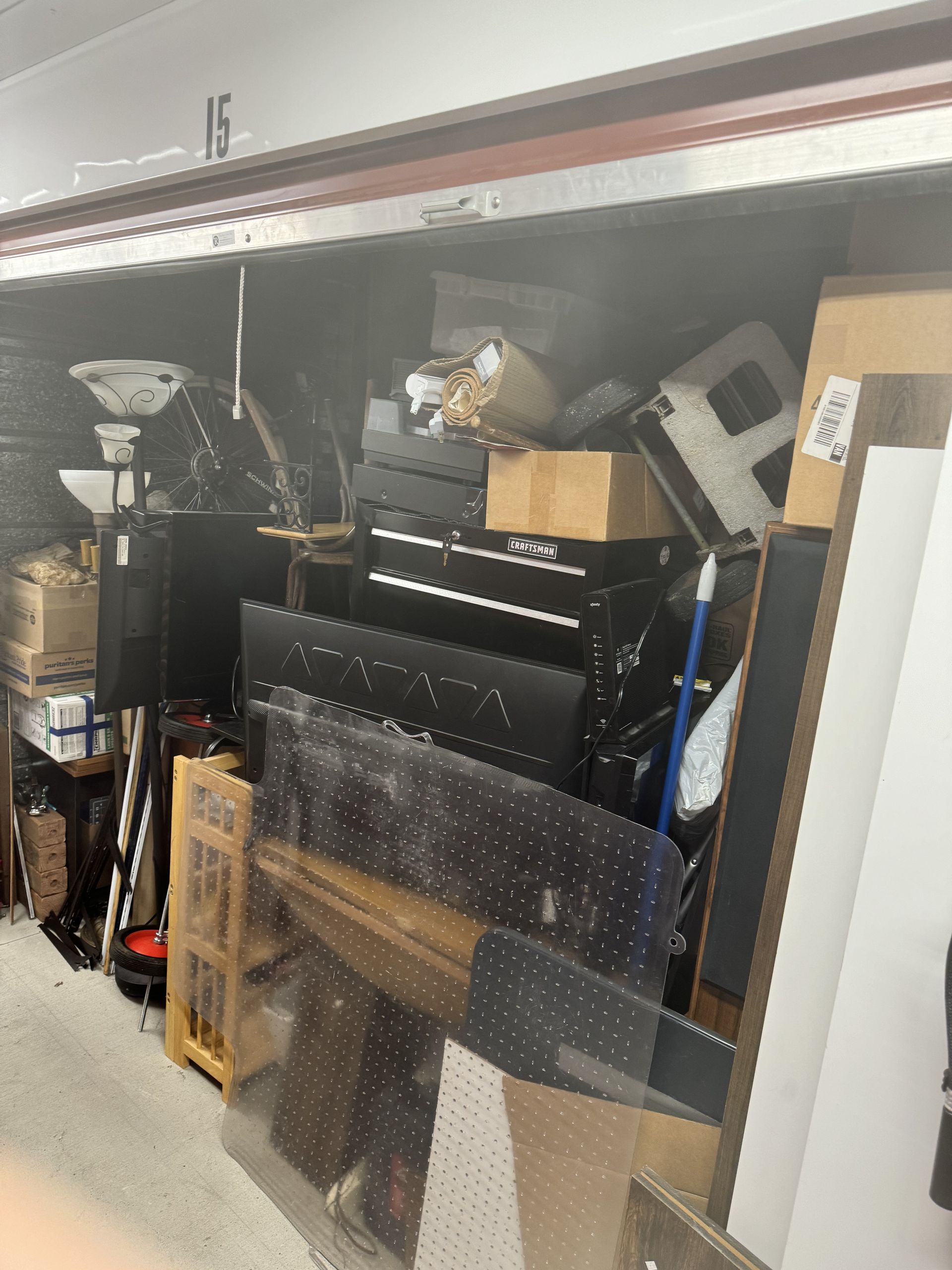 Storage unit packed with furniture, boxes, and various items. Interior is dark and cluttered.