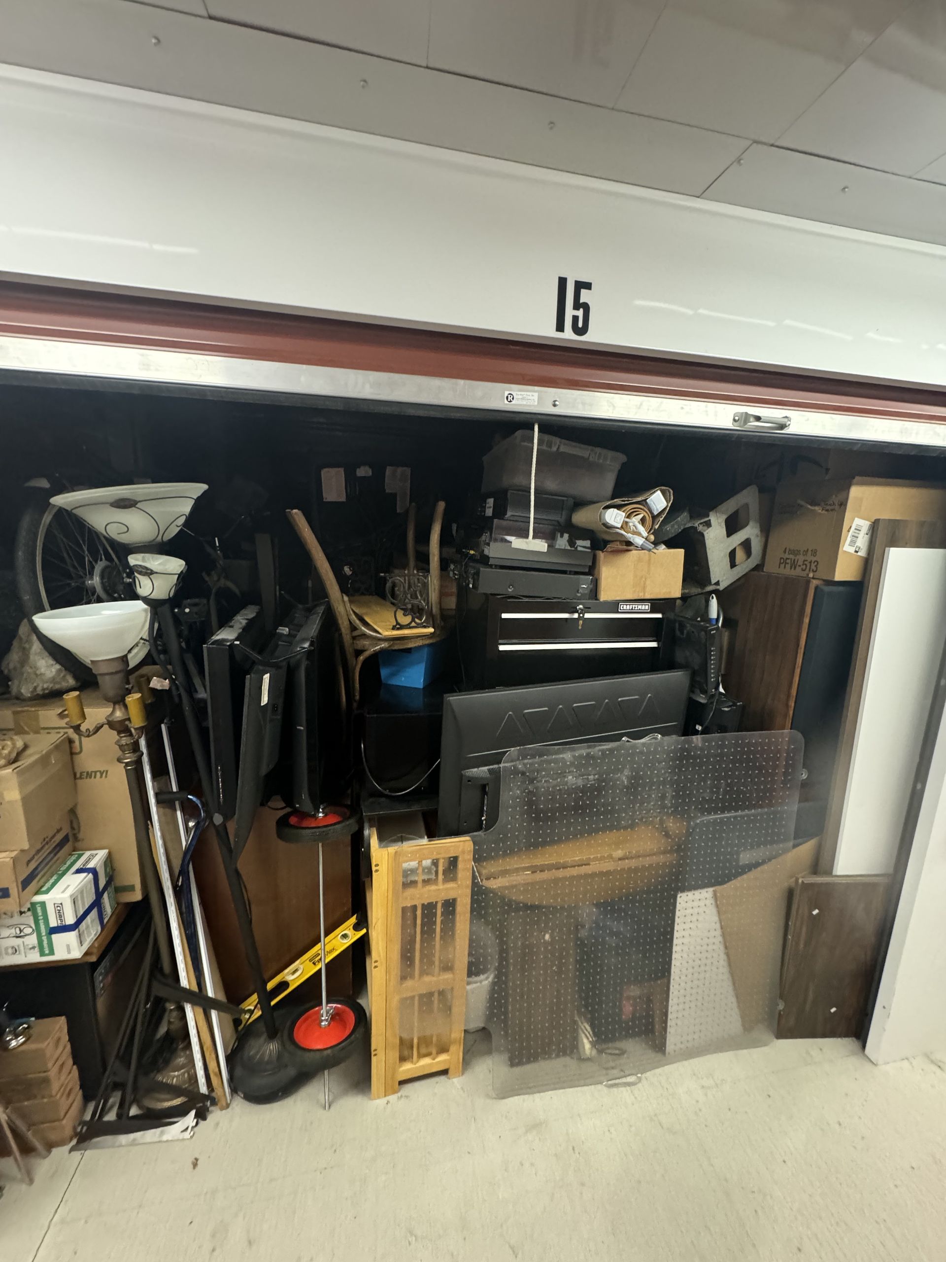 A cluttered storage unit filled with various items, including boxes, furniture, and tools.
