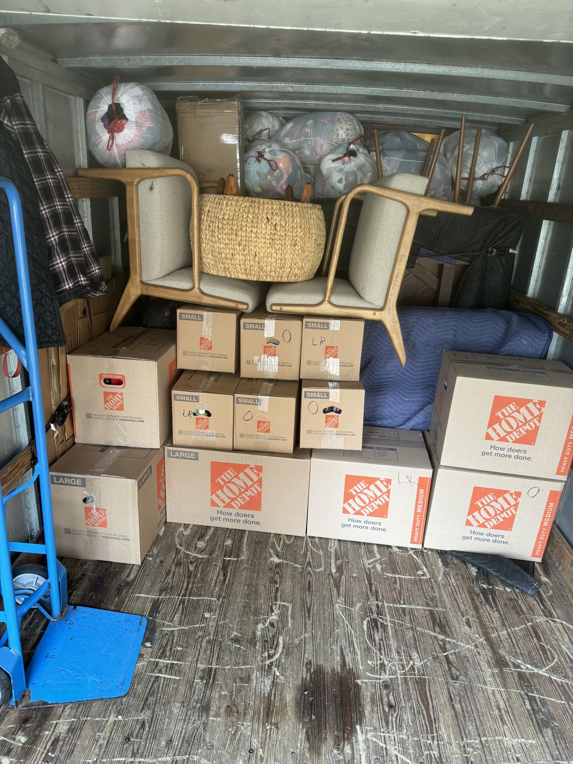 Boxes and furniture loaded into a moving truck. Includes two chairs, a basket, and a dolly.