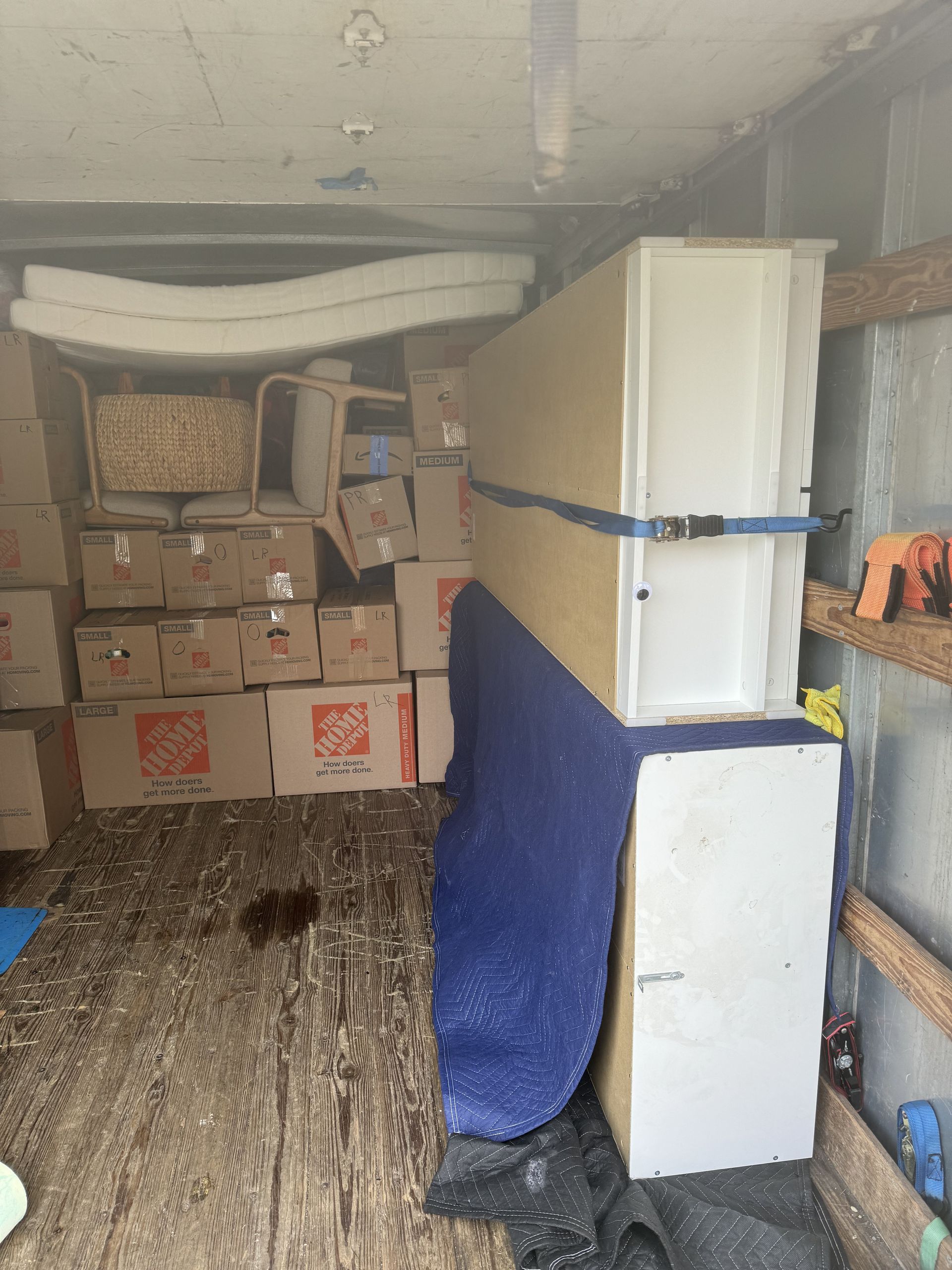 Inside a cluttered truck: boxes, large white panel secured with a blue strap, and foam packing material.