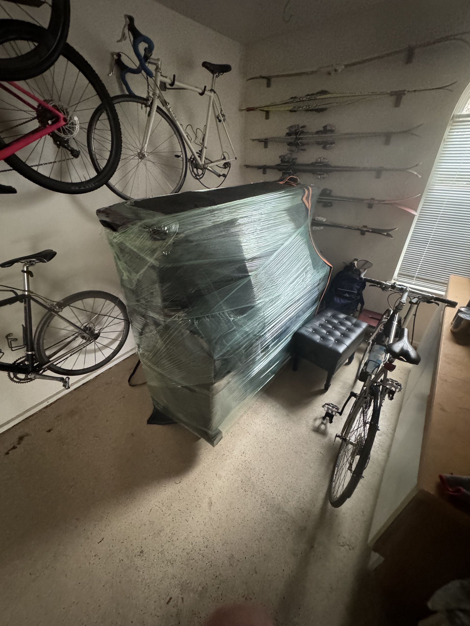 A wrapped piano in a room with bicycles on the wall and a chair next to it.