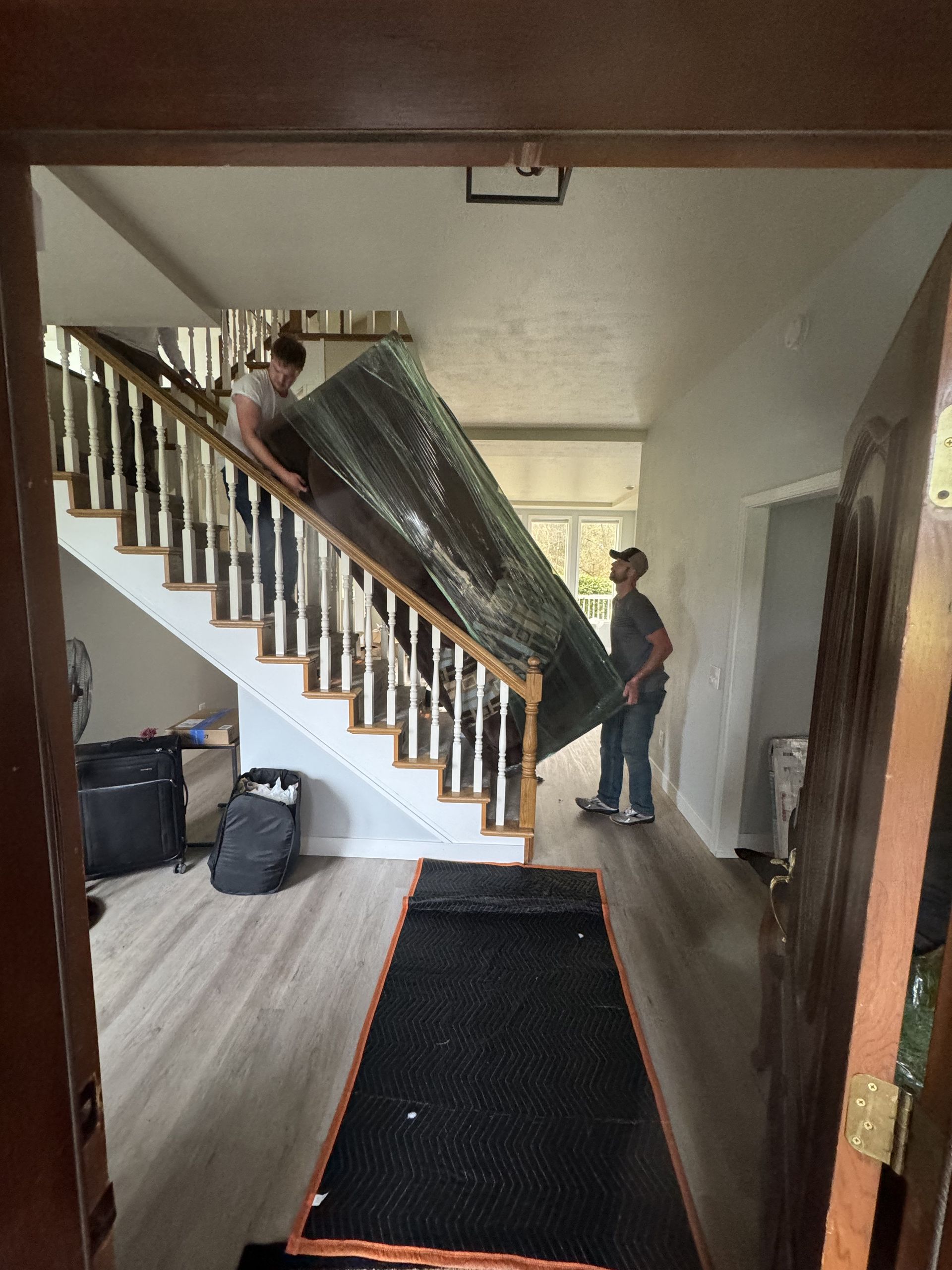 Two people moving a large, wrapped object up a staircase into a home's entryway.