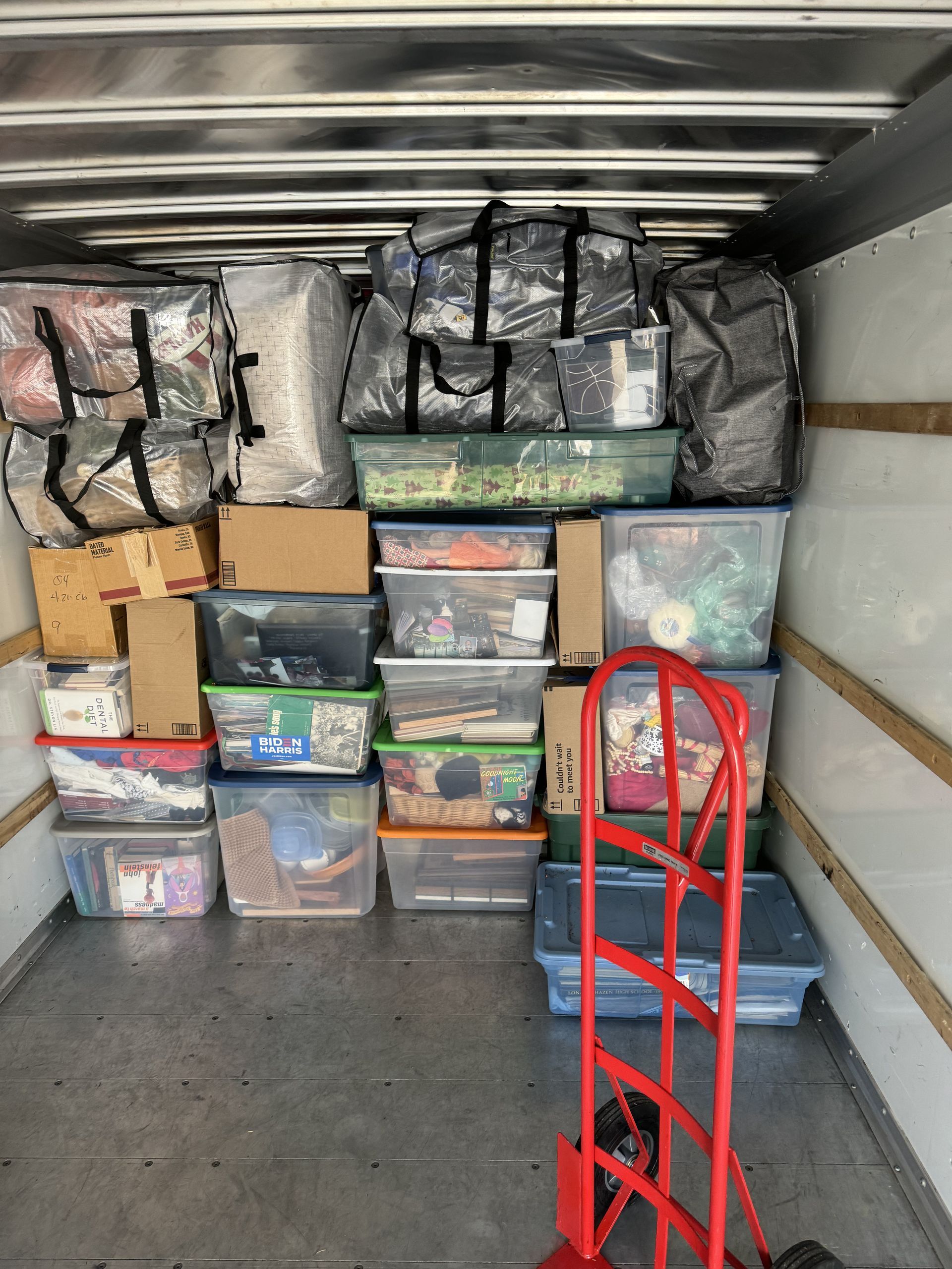 A packed moving truck interior: totes, bags, boxes, and a dolly fill the space.