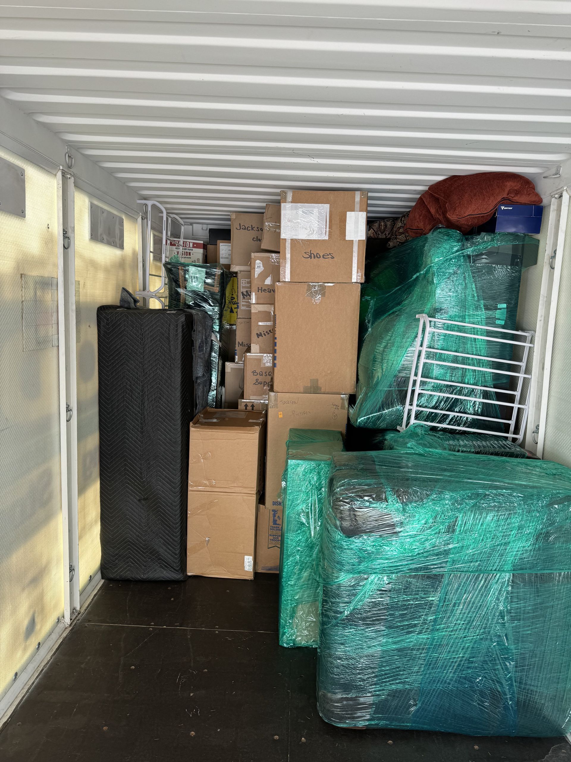 Inside of a packed moving truck, filled with boxes and wrapped furniture.