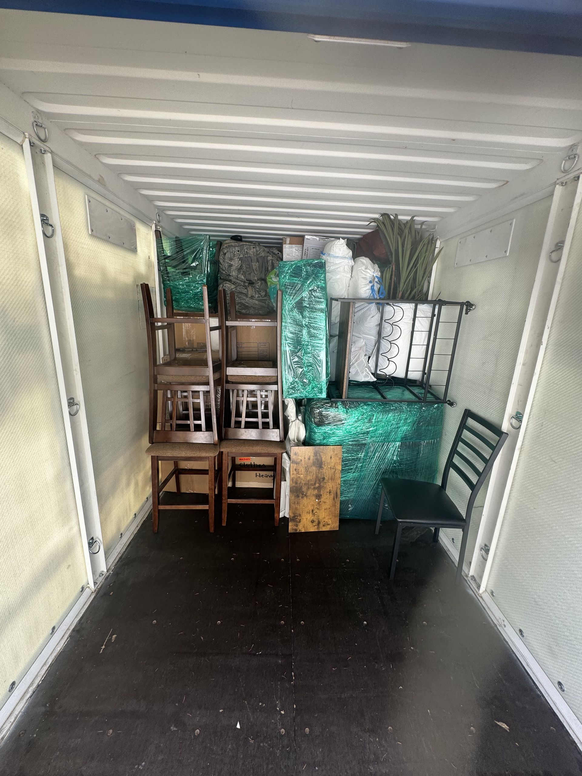 Inside of a cargo container filled with packed furniture, chairs, and other items.