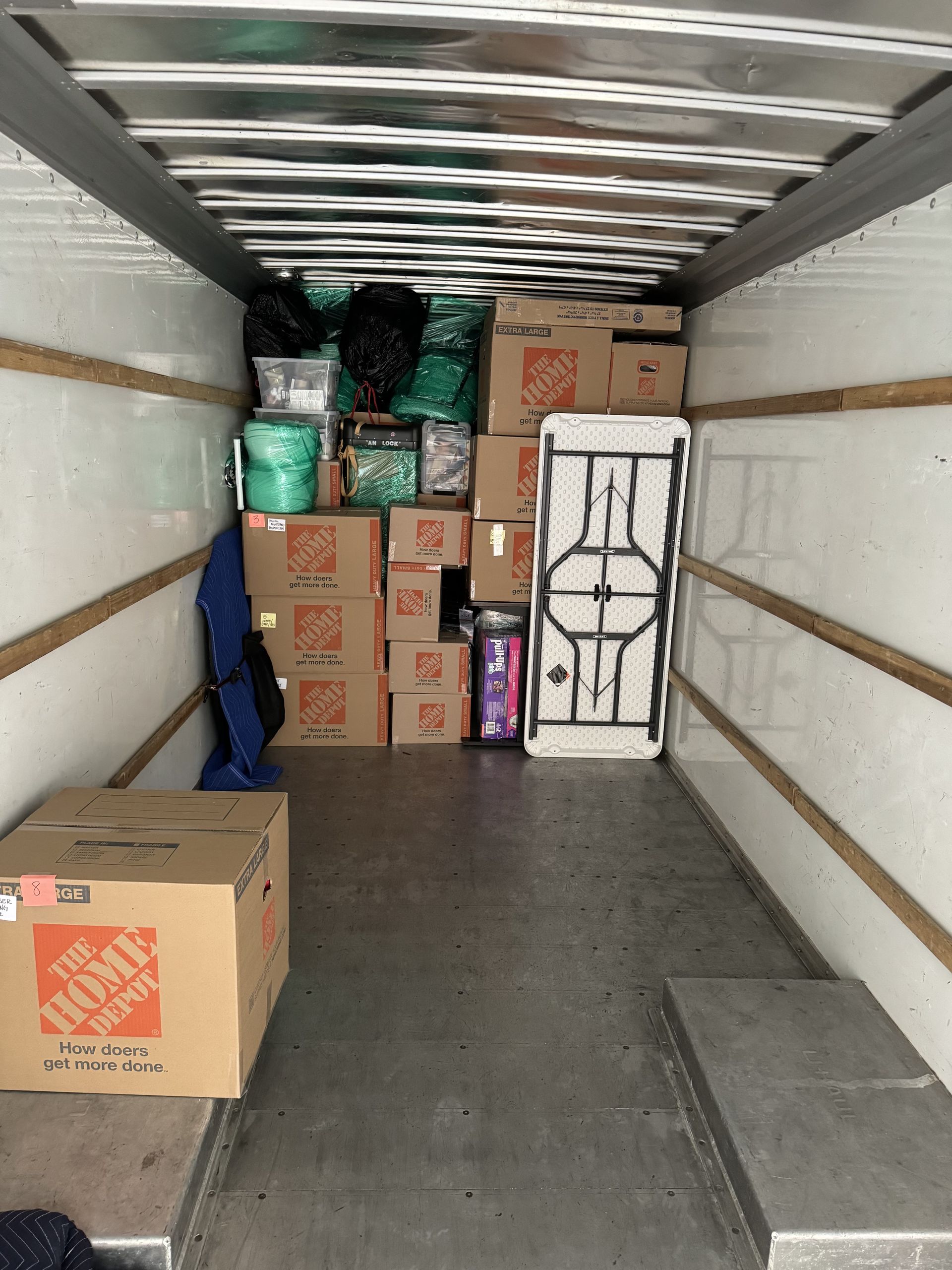 Moving truck interior filled with cardboard boxes and miscellaneous items, including a folding table.