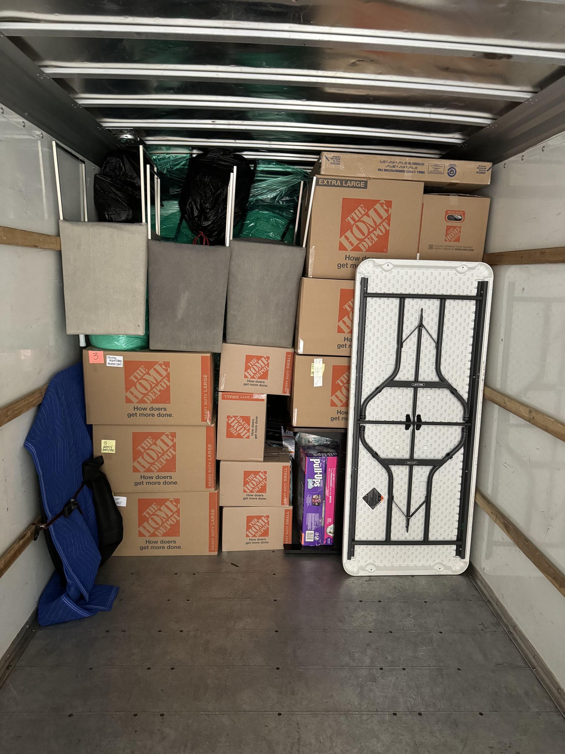 A moving truck interior filled with packed boxes, furniture, and wrapped items.