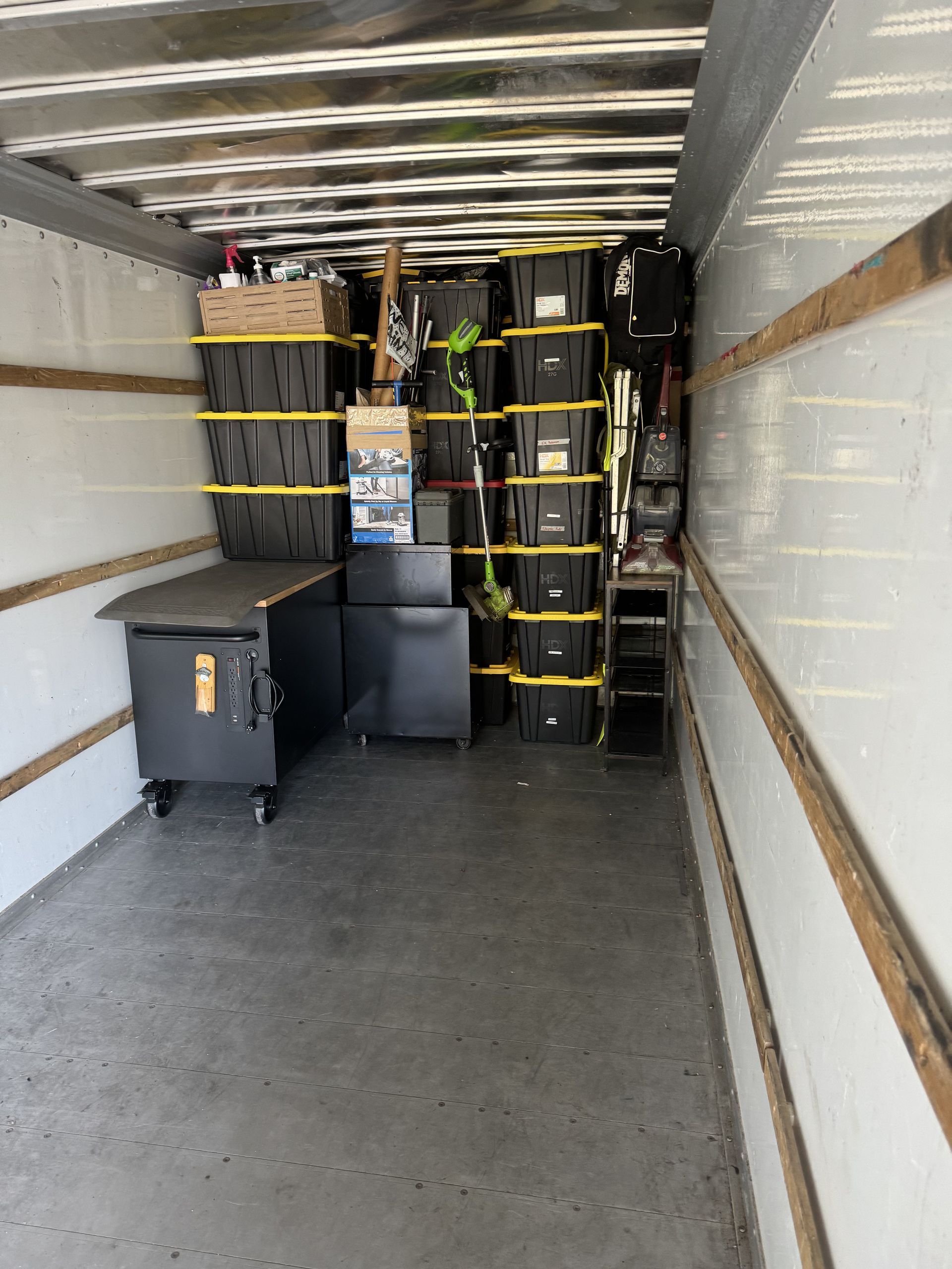 Inside a moving truck packed with black crates secured by yellow straps and other items.