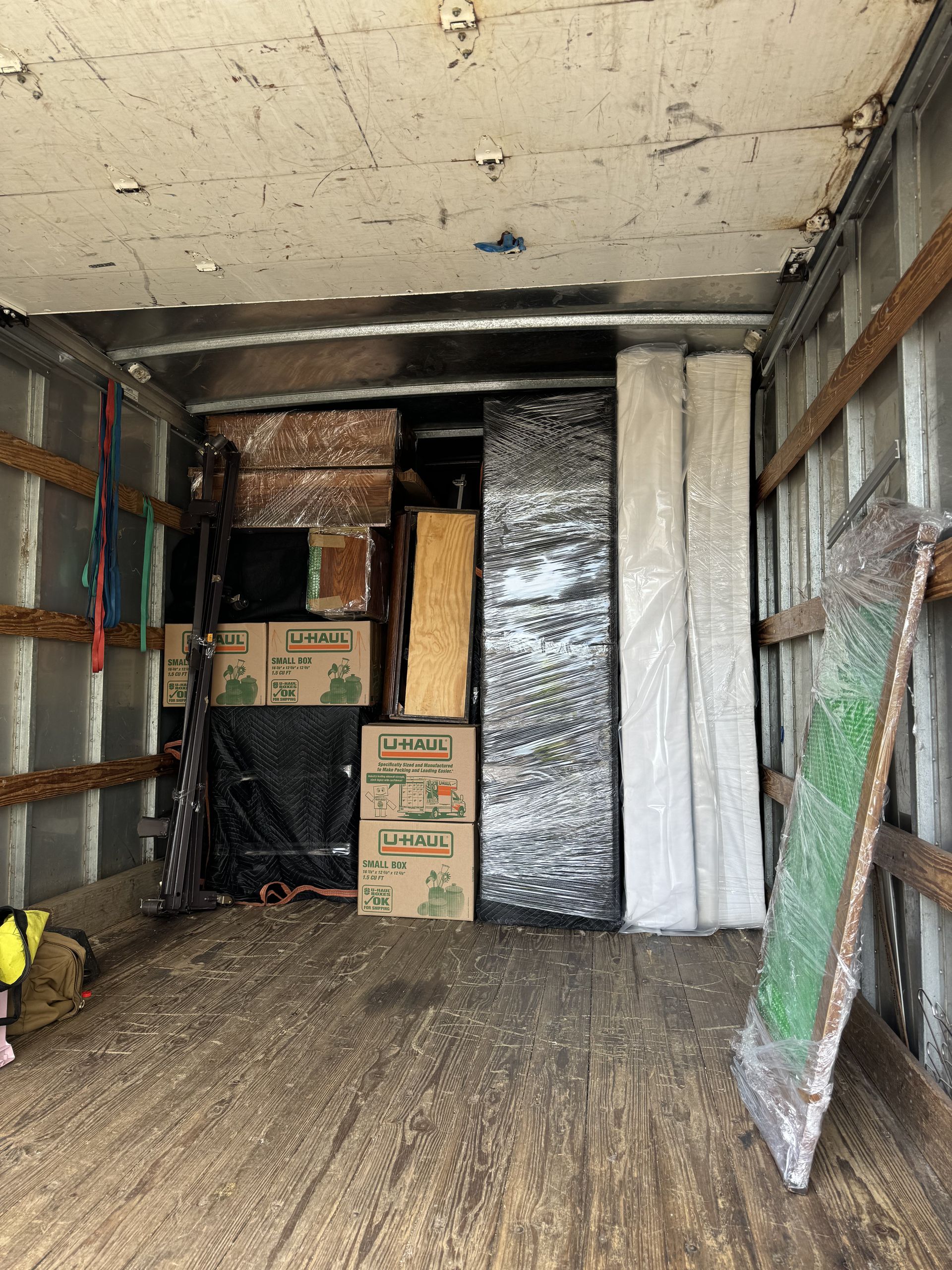 Inside of a moving truck filled with boxes, furniture wrapped in plastic, and a large mirror.