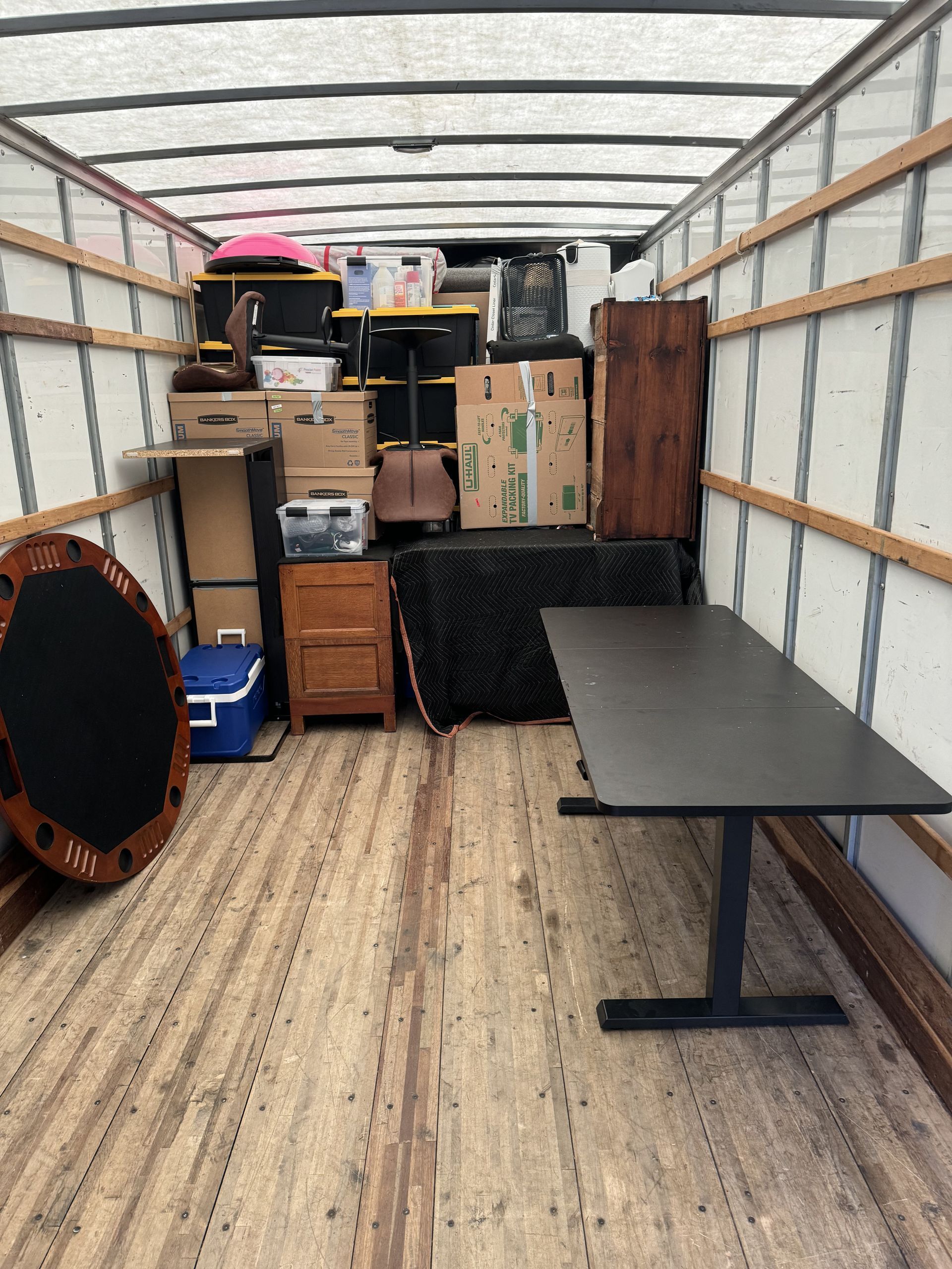 Interior of a moving truck packed with furniture and boxes, including a table, cabinet, and round game table.