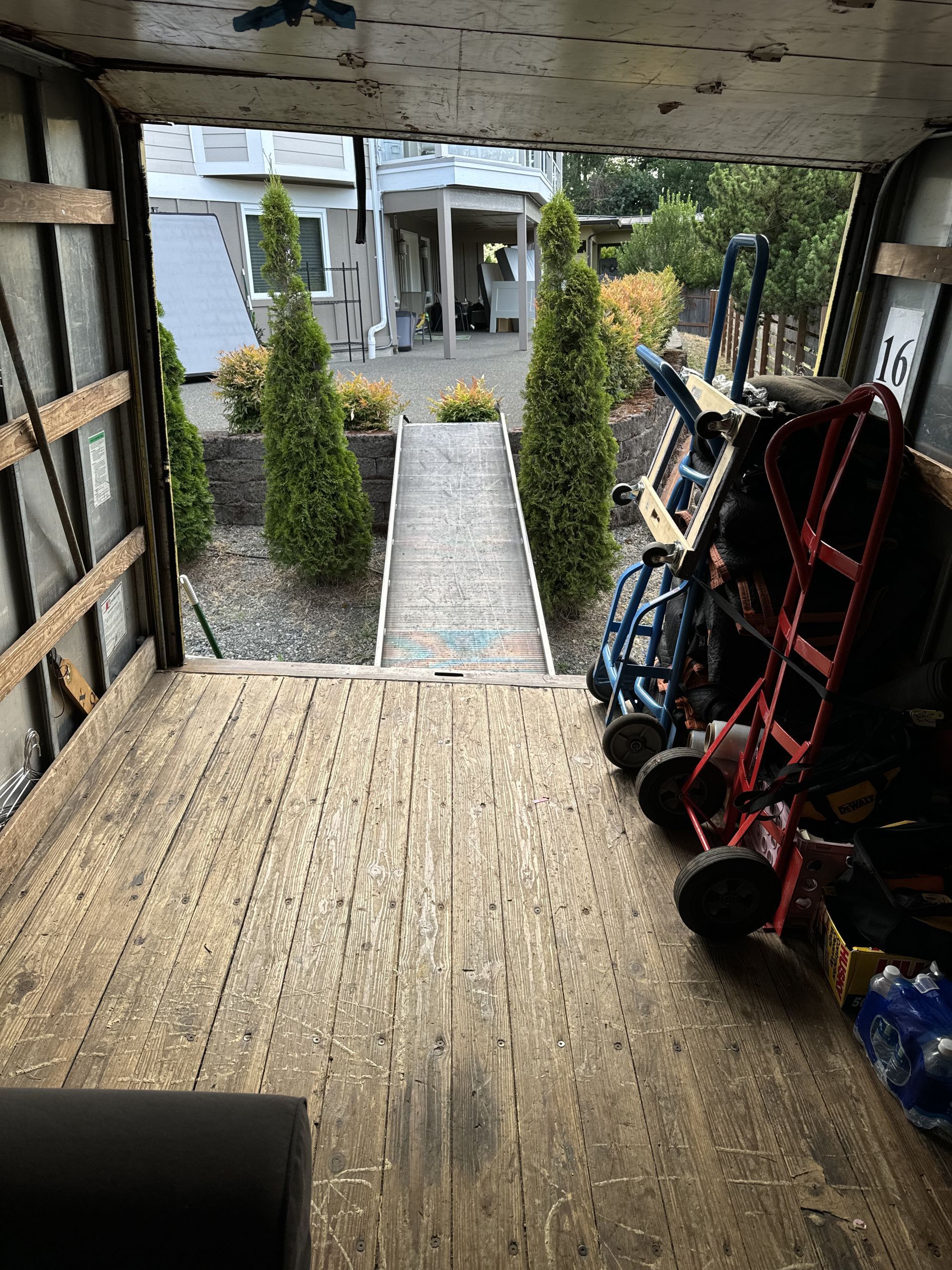 Inside a moving truck, ramps face a walkway with trees. Dollies and equipment are loaded.