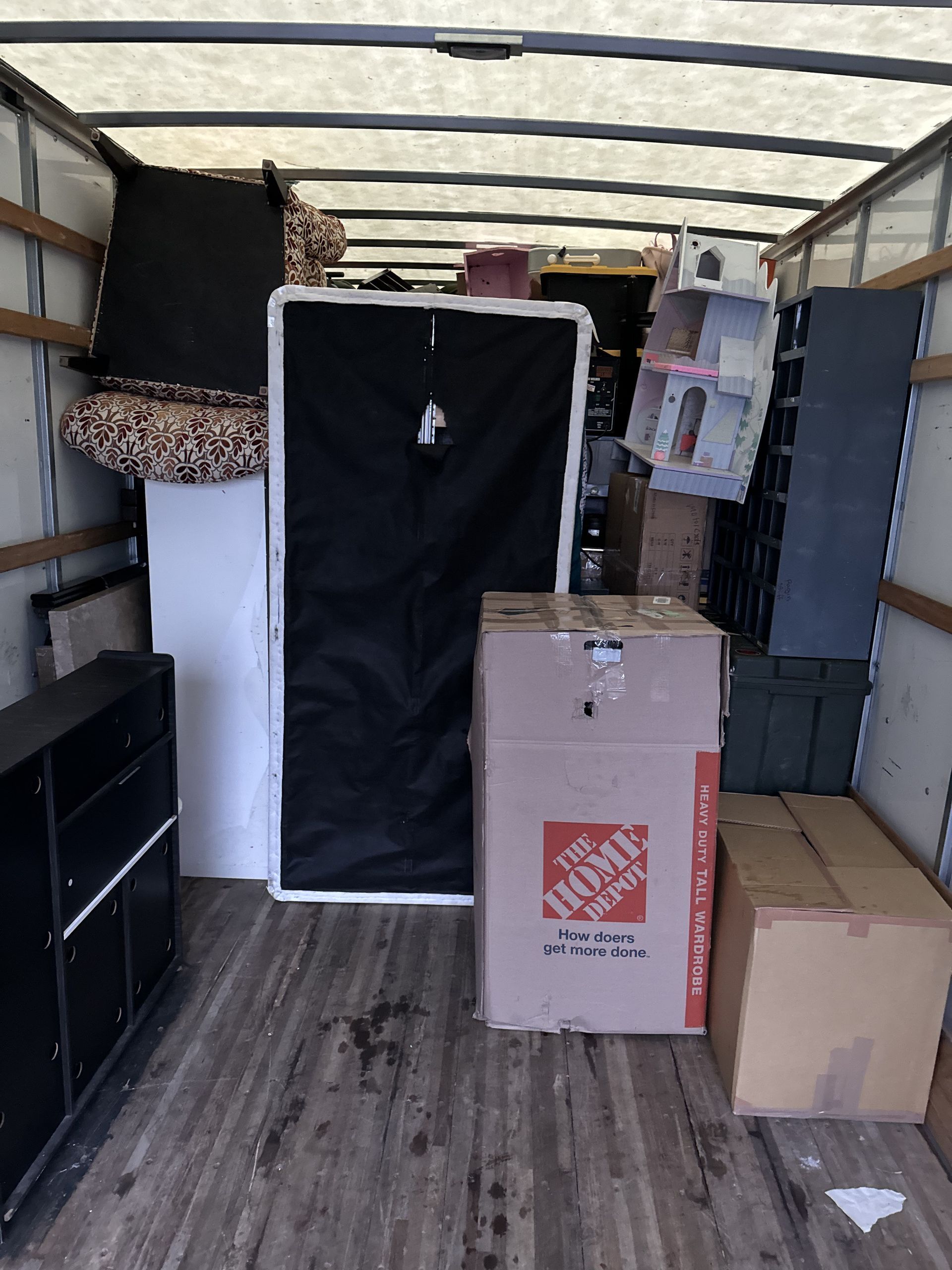 Moving truck interior packed with furniture, boxes, and a large black object.