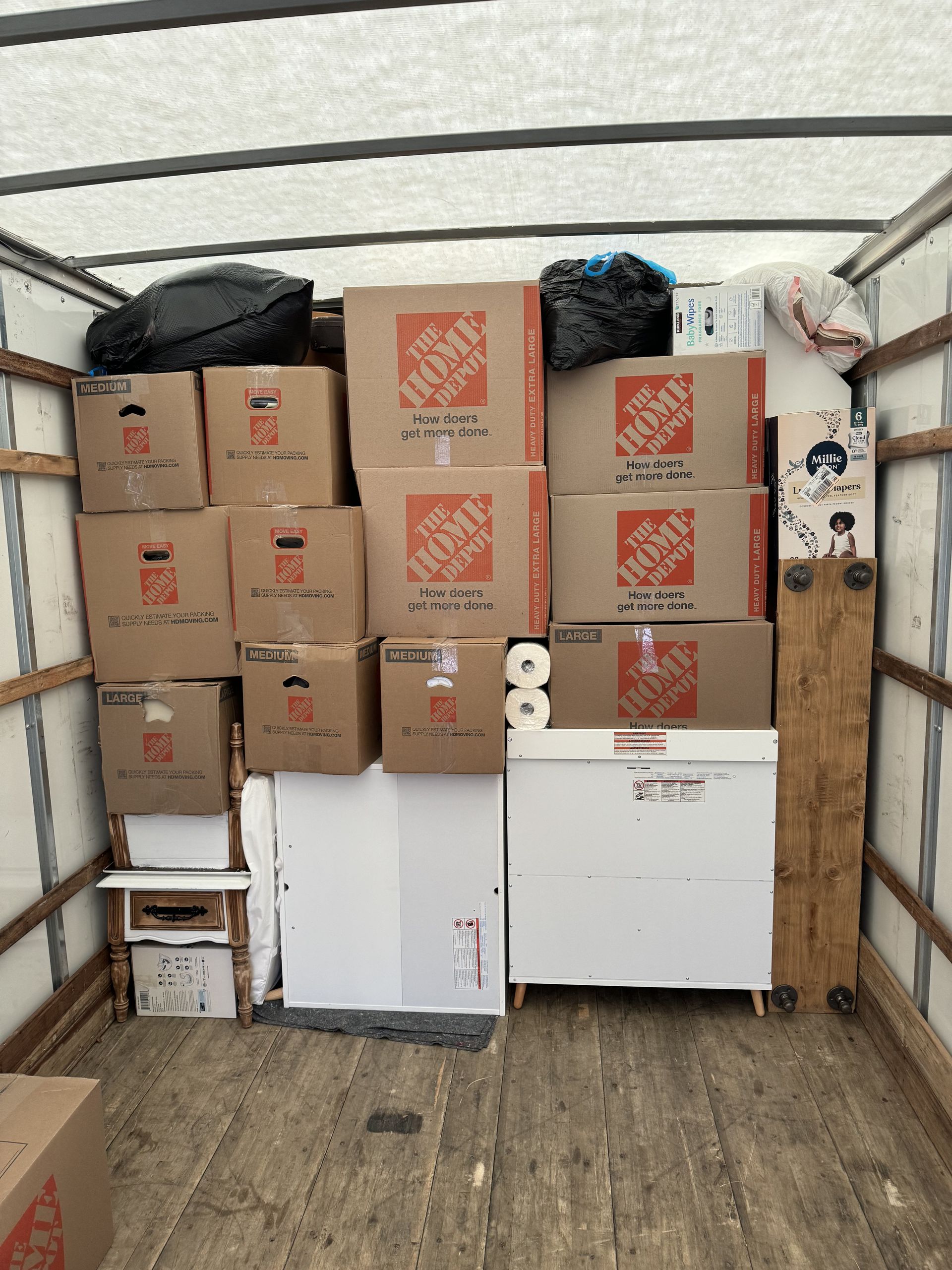 Boxes and furniture fill the back of a moving truck; brown boxes stacked high, with a white cabinet on the right.