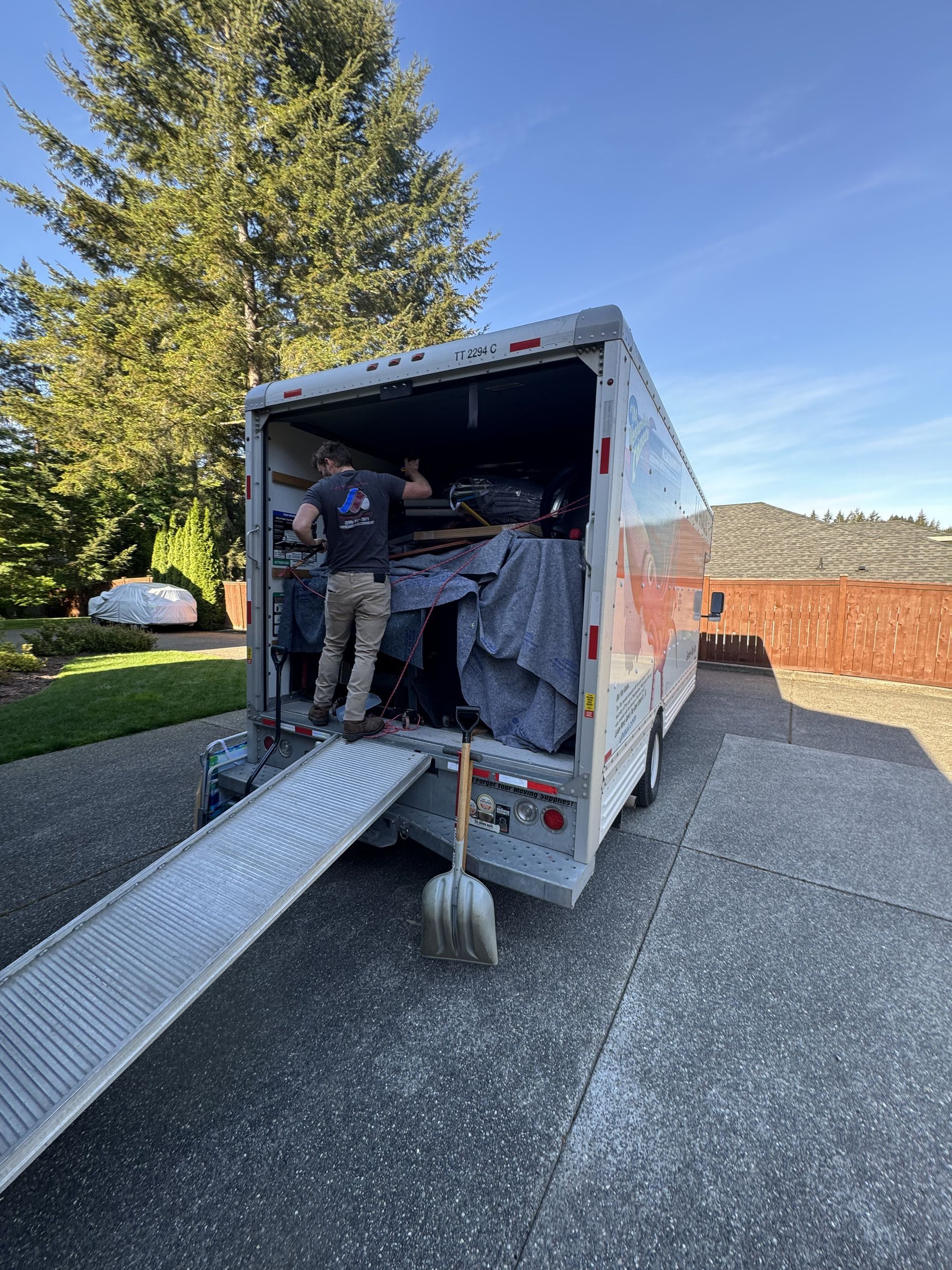 Man loading furniture into a trailer with a ramp on a driveway.