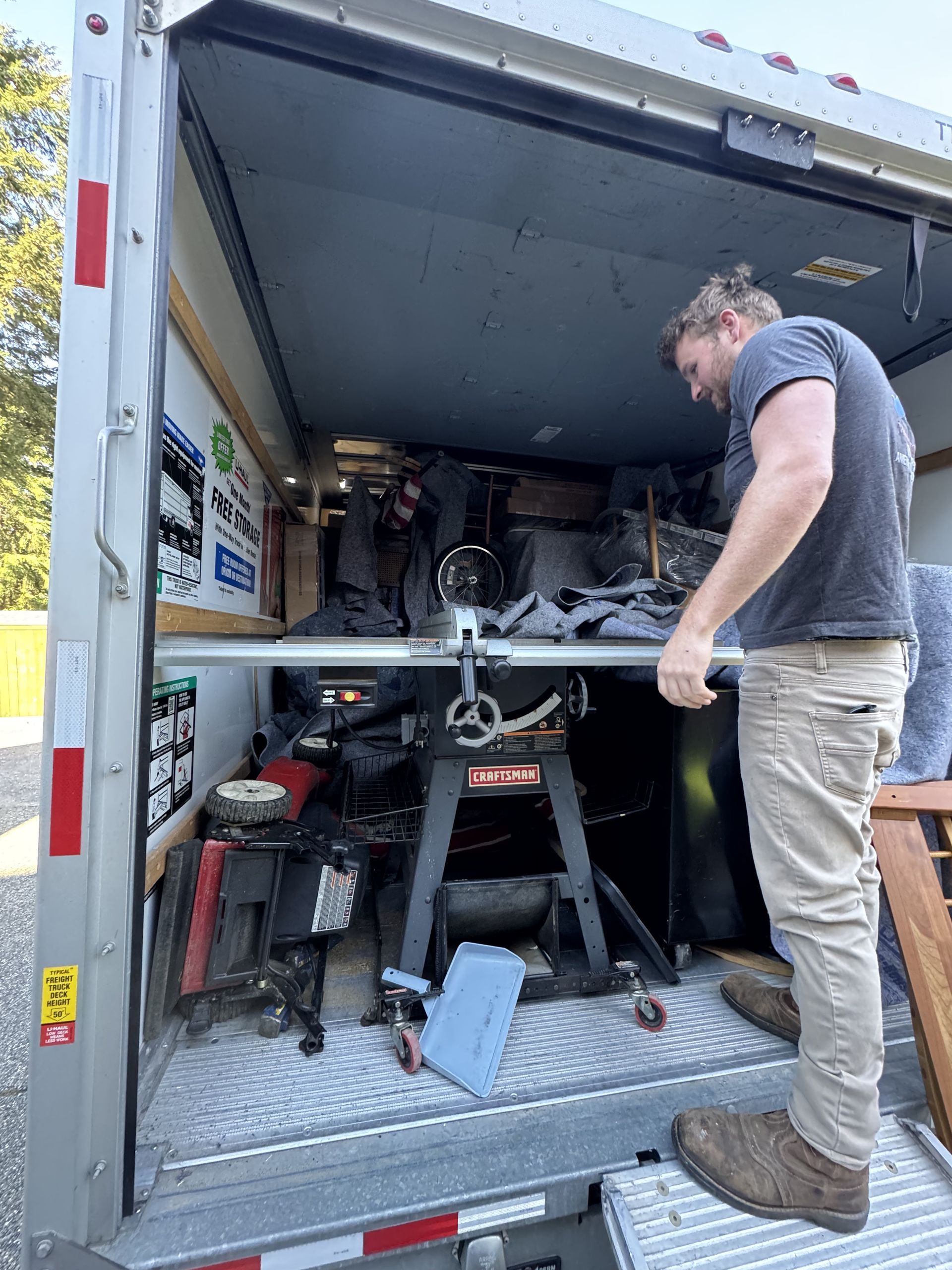 Man in truck looking at a table saw and other items. Truck interior is visible.