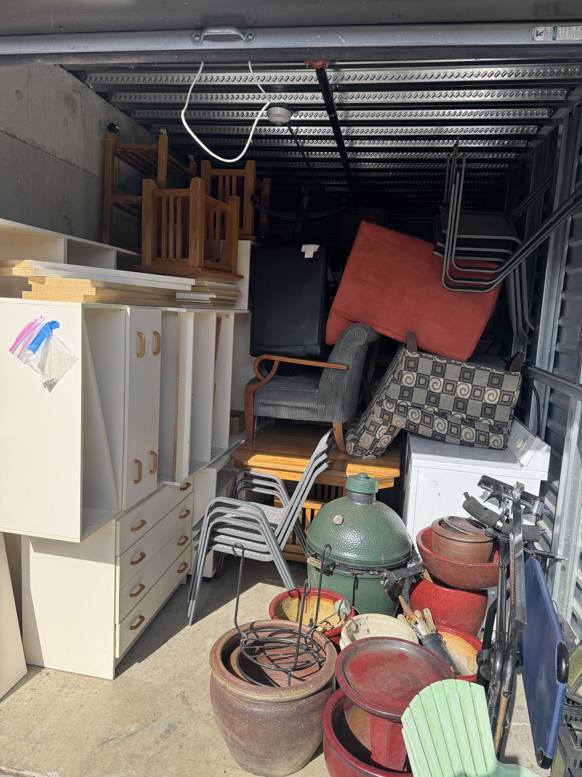 A cluttered storage unit. Furniture, pillows, and planters are piled inside.